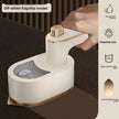 White handheld steamer with gold accents on a dark surface, held by a hand.
