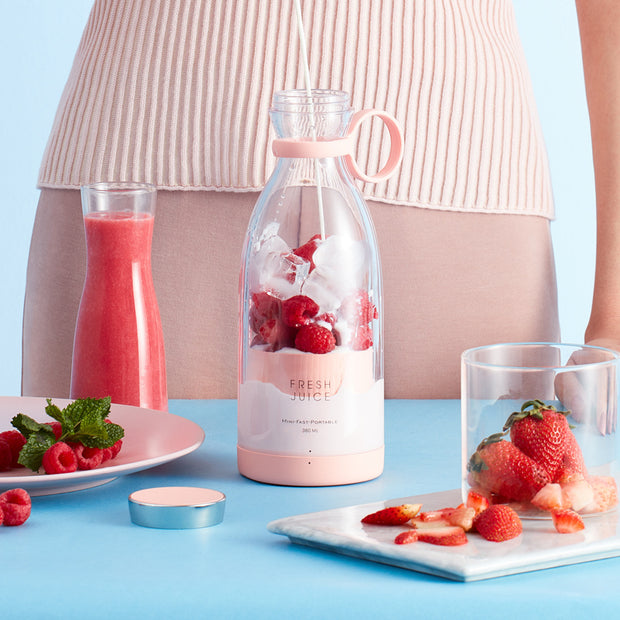 Bottle of fresh juice with strawberries and raspberries on a blue table, with a person in a striped shirt partially visible.