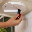 Hand using a red tool to adjust or fix a ceiling light fixture.