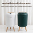 Two trash bins, one white and one green, on a light wooden floor with a white curtain background.