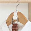 White clip attached to a brown leather belt on a wooden hanger against a white background