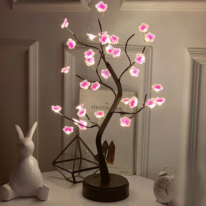 Decorative LED tree with pink flowers on a table next to a rabbit figurine and books.