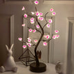 Decorative LED tree with pink flowers on a table next to a rabbit figurine and books.