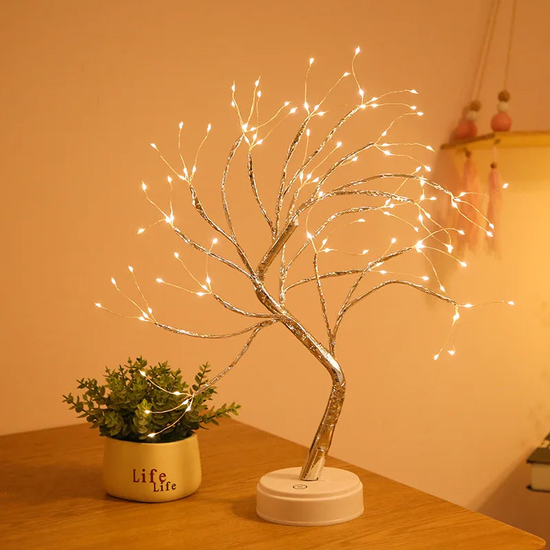 Decorative LED tree with lights on a wooden surface next to a small potted plant.
