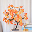 Decorative lamp with orange leaves on a table next to books and a candle.