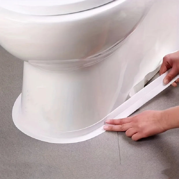 Person applying a white strip to the base of a toilet on a gray floor.