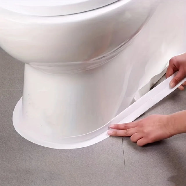 Person applying a white strip to the base of a toilet on a gray floor.