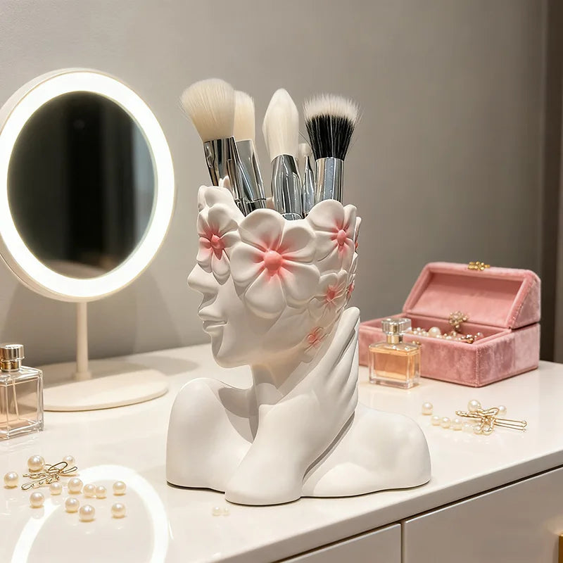 Makeup brush holder shaped like a face with flowers, placed on a vanity table with makeup items.