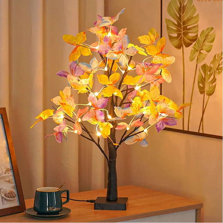 Decorative LED tree with colorful leaves on a wooden table next to a mug.