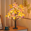 Decorative LED tree with colorful leaves on a wooden table next to a mug.