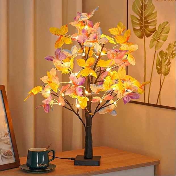 Decorative LED tree with colorful leaves on a wooden table next to a mug.