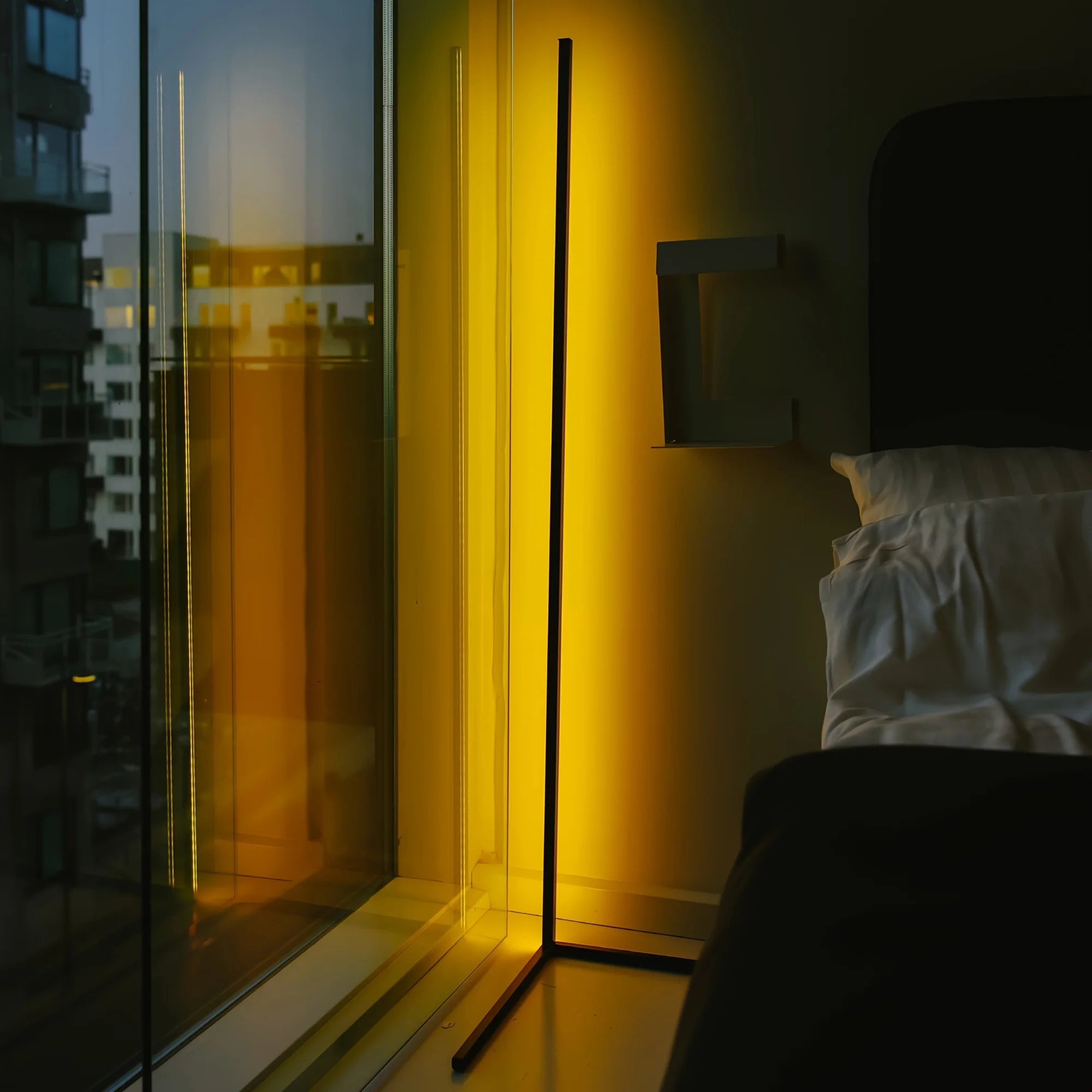 Modern bedroom with a floor lamp casting a warm glow near a window with a cityscape view.