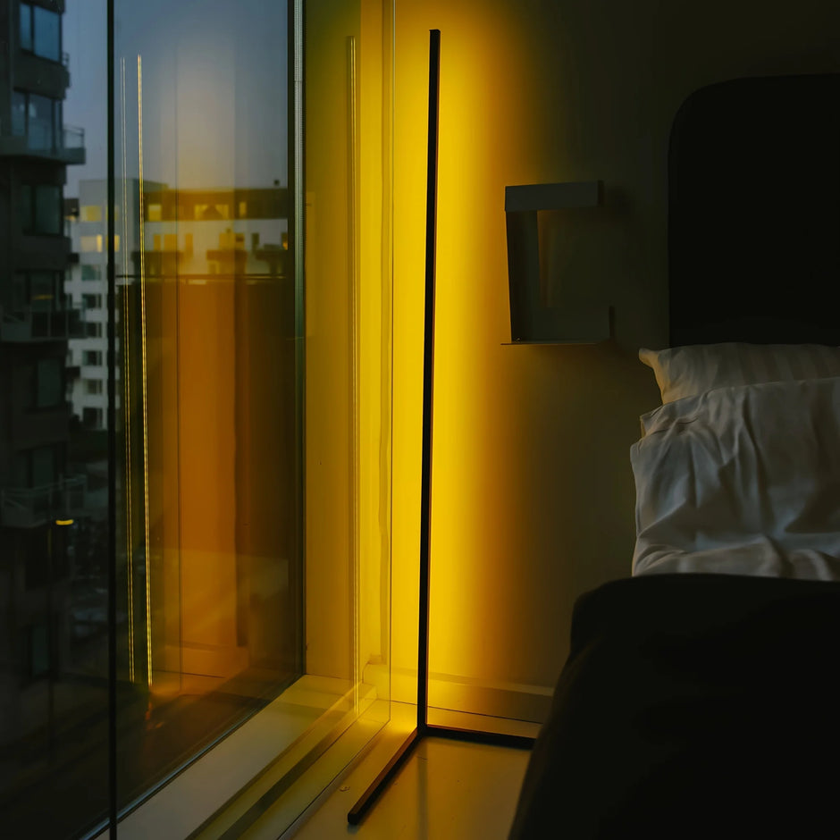 Modern bedroom with a floor lamp casting a warm glow near a window with a cityscape view.