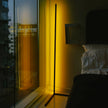 Modern bedroom with a floor lamp casting a warm glow near a window with a cityscape view.