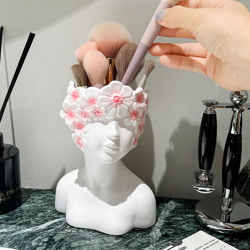 White bust-shaped brush holder with floral design holding makeup brushes on a marble surface.
