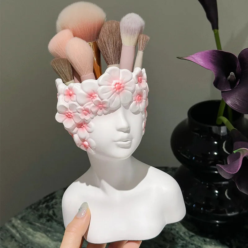 White bust-shaped makeup brush holder with floral design holding makeup brushes, against a neutral background.
