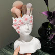 White bust-shaped makeup brush holder with floral design holding makeup brushes, against a neutral background.