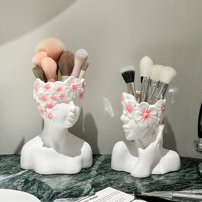 Two white ceramic brush holders shaped like faces with floral designs on a marble surface.