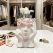White ceramic holder shaped like a face with makeup brushes in a closet setting