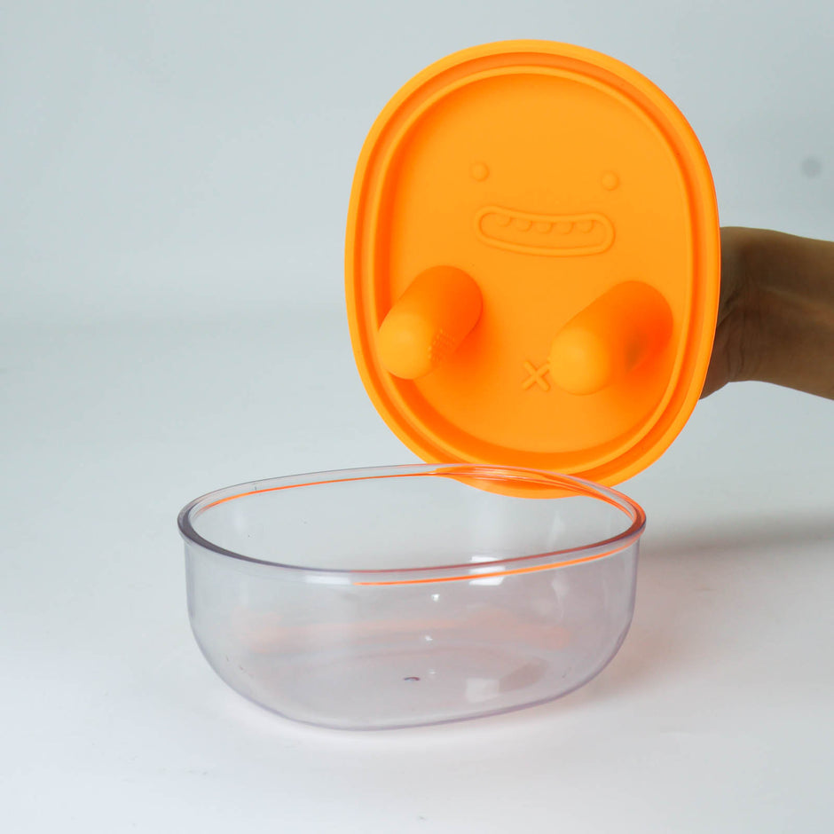 Clear glass bowl with an orange lid on a white background