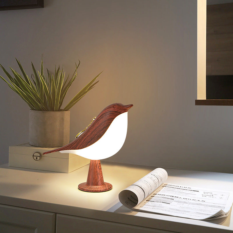 Bird-shaped table lamp on a desk with a plant and newspaper in the background