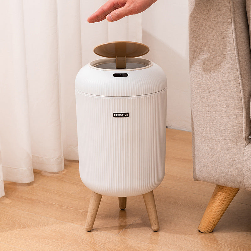 White trash bin with wooden legs on a wooden floor next to a beige chair.