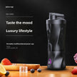 Black portable juicer cup on a wooden surface with fruits and ice cubes, against a dark background.