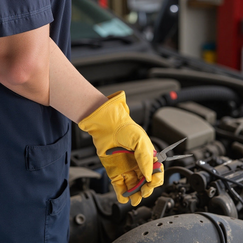 Person wearing a yellow glove holding pliers with an engine in the background