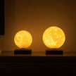 Two moon-shaped lamps on a dark surface with a warm glow.