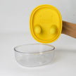 Clear glass bowl with a yellow lid on a white background